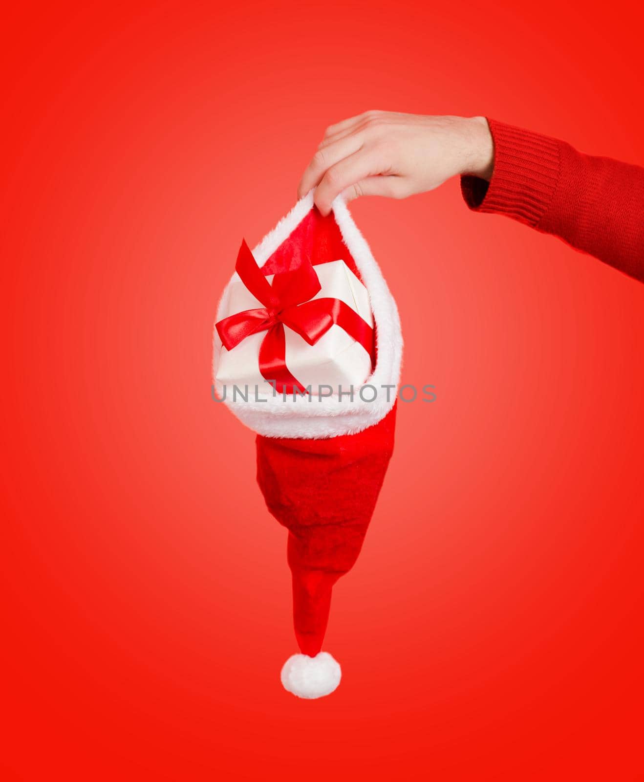 Human hand is holding santa hat with gift box on a red background