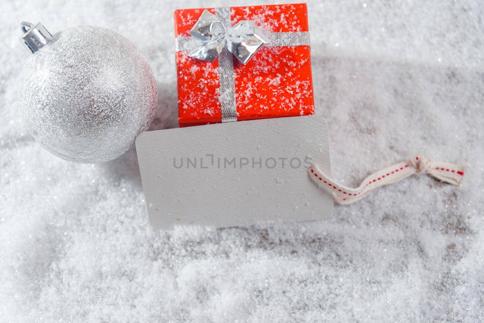 Gift box, white ball and card in the snow, space for text