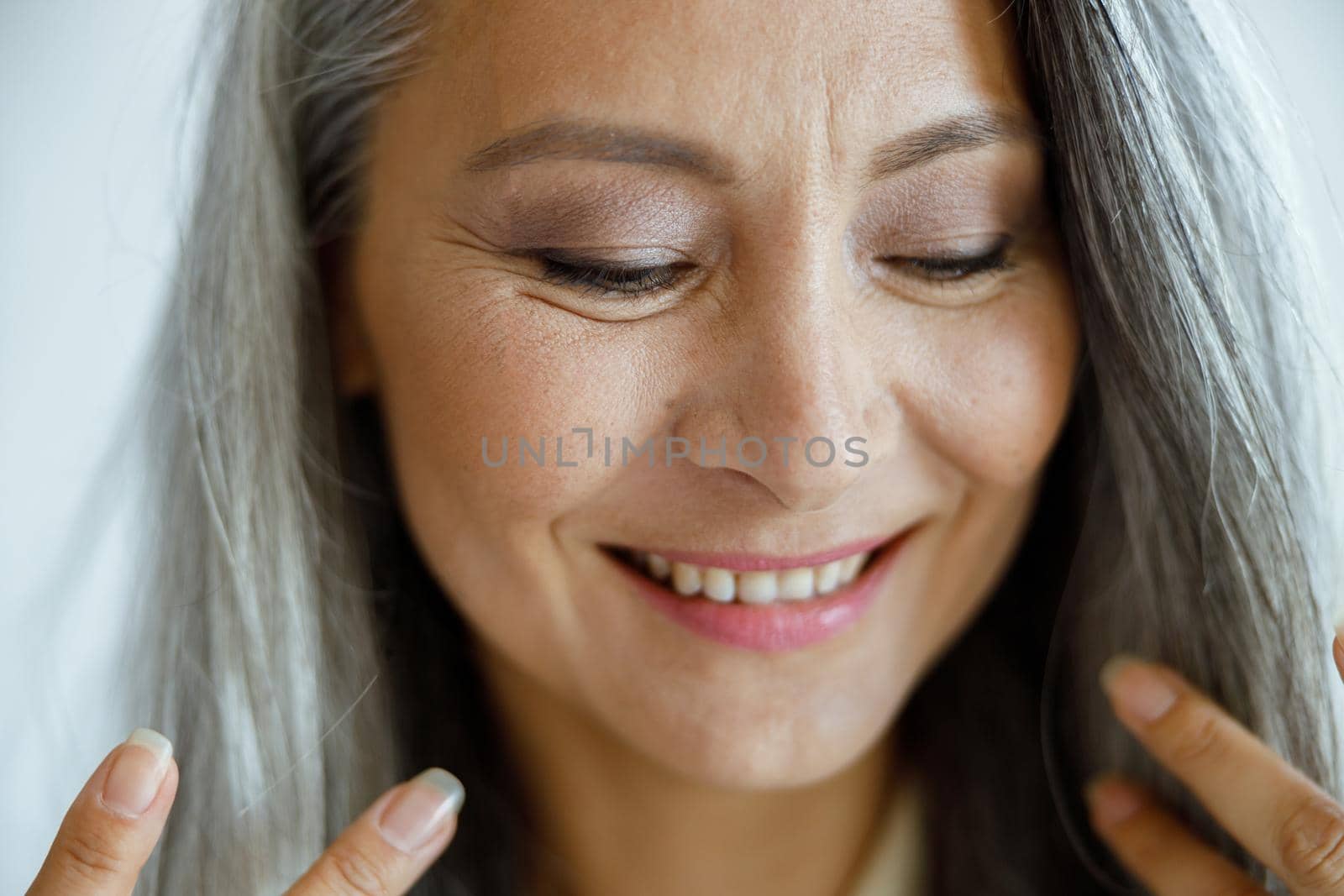 Cute middle aged Asian female model with loose grey hair poses on light background in studio closeup. Mature beauty lifestyle