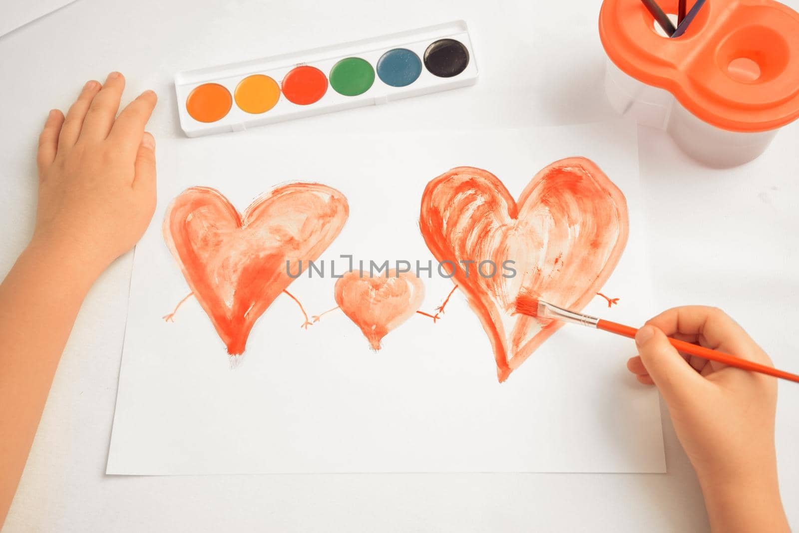 Unrecognizable child paints three red hearts, concept of family