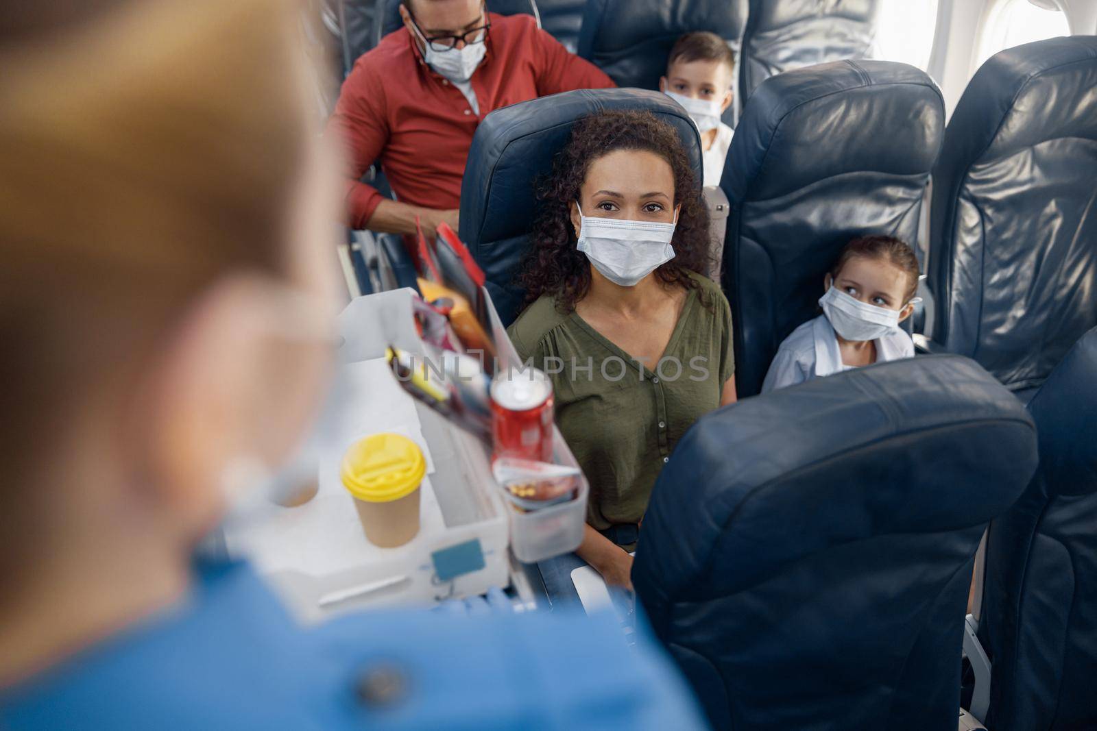 Female passenger with little daughter wearing protective face masks waiting for stewardess to order coffee during the flight. Covid19, travel, service, transportation concept. Selective focus