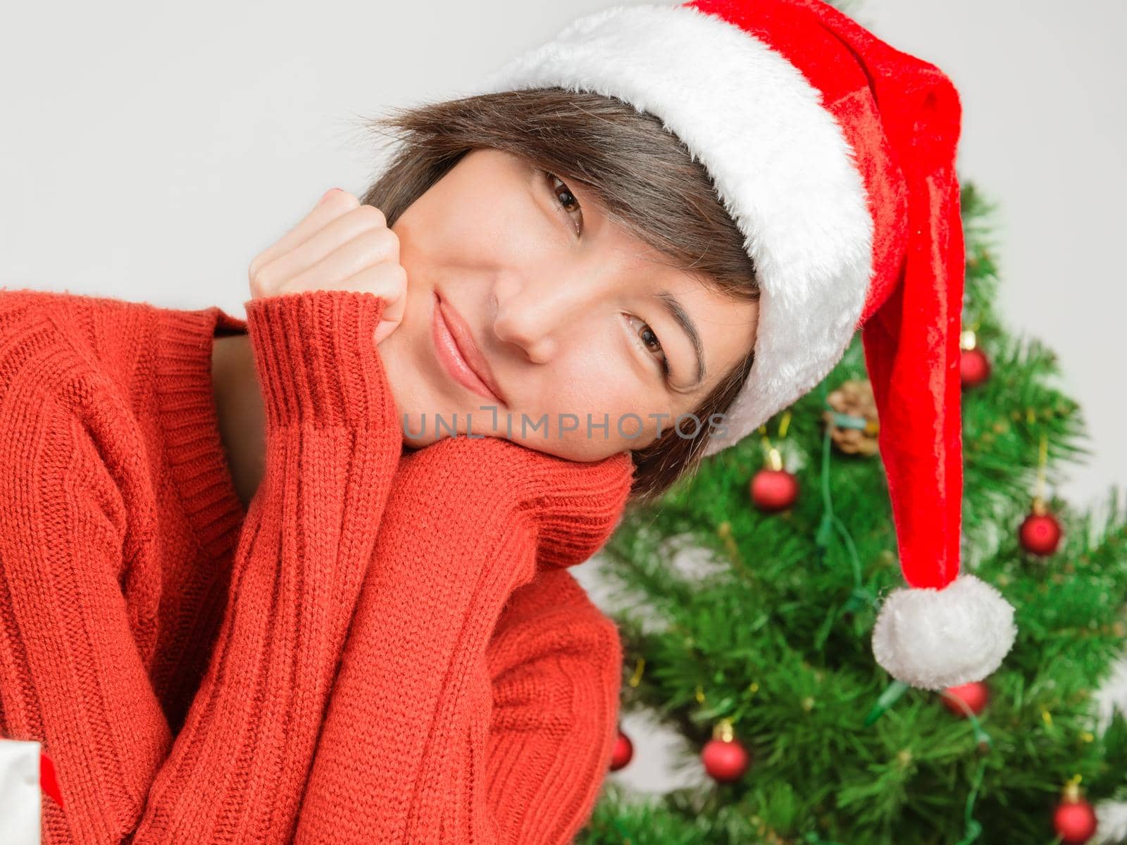 Beautiful woman in a santa hat smiling on the background of Christmas tree