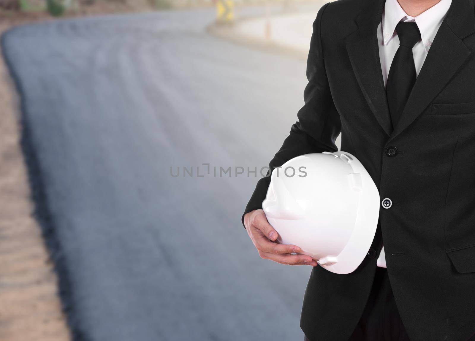 engineer in suit holding helmet with asphalt road under construction  by geargodz