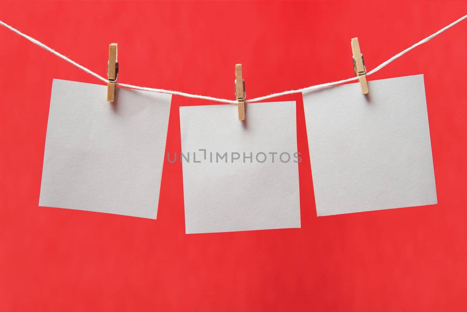 Sheets of paper on a clothespins on a red background, space for text