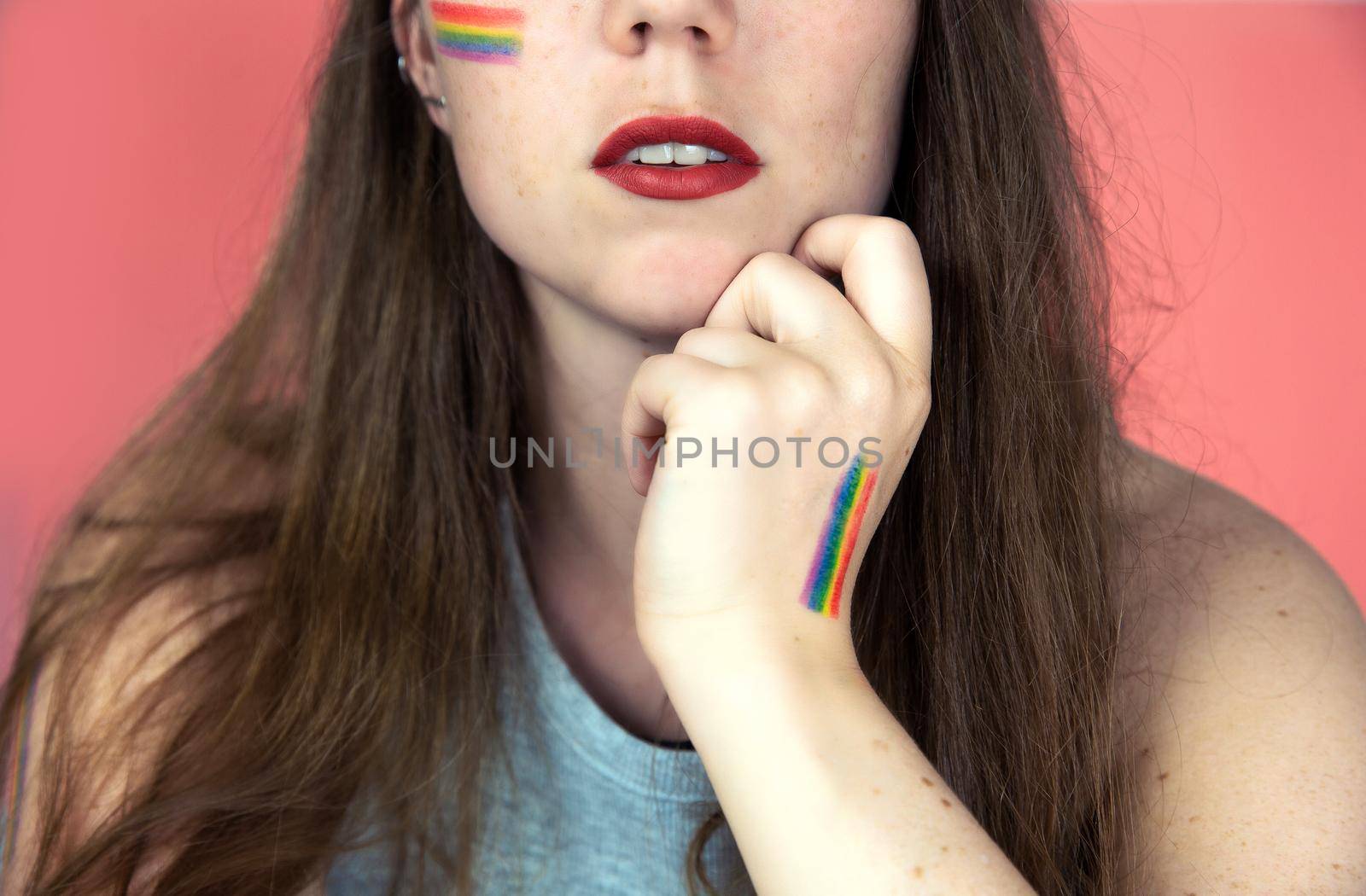 Portrait of a young woman with rainbow Flag on cheek and body, the LGBT community on a colorful pink background by Annebel146