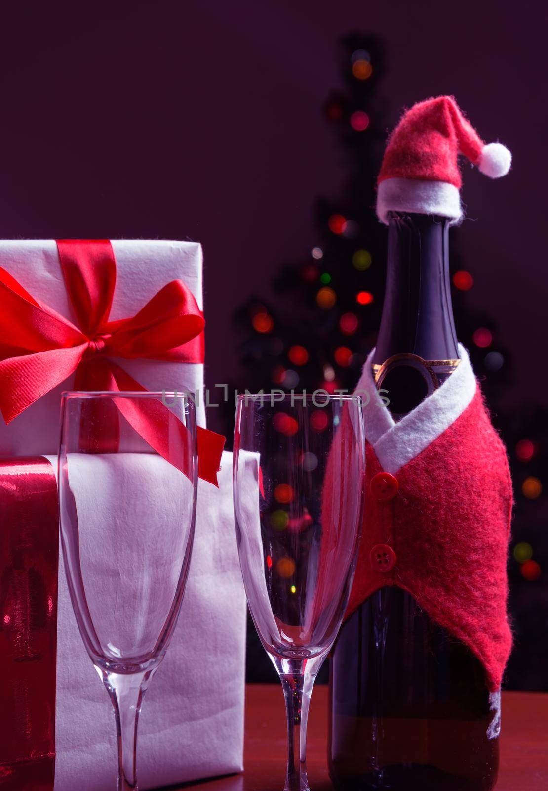Bottle of champagne, glasses, gift boxes on the background of Christmas tree