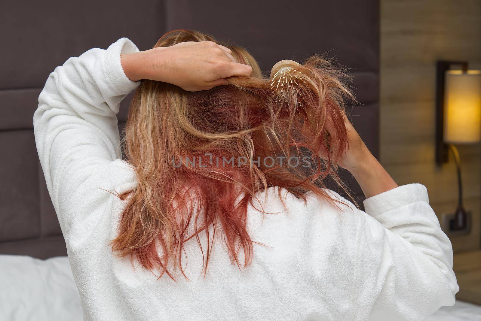 a blonde with dyed hair combing her tangled hair after a shower with a wooden comb. by PhotoTime