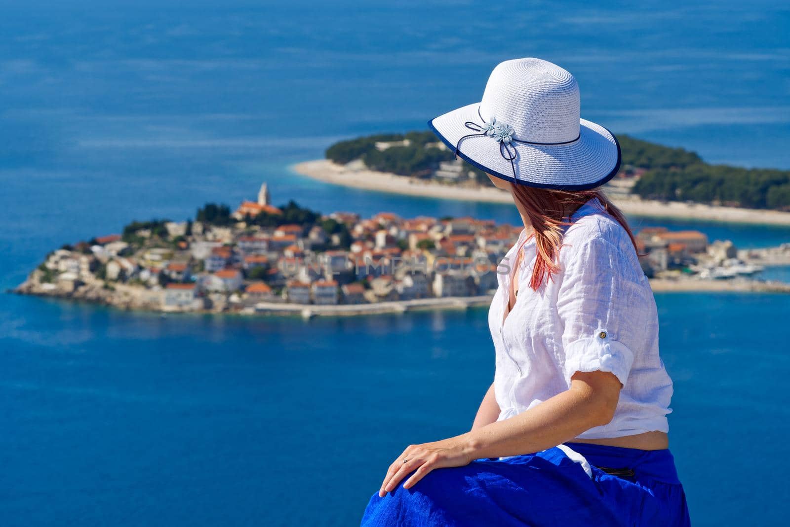 Beautiful tourist woman in a white straw hat on beautiful blue Adriatic Sea and cozy island background. Croatia during summer holiday. Luxury life at holiday at turquoise sea, ocean. Travel concept, Greece