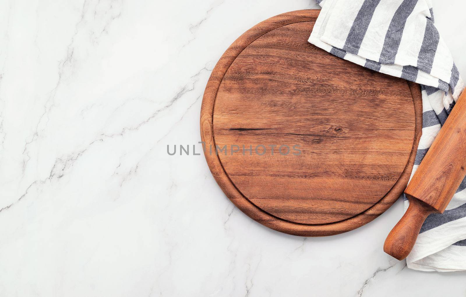 Empty wooden pizza platter with napkin and rolling pin set up on marble stone kitchen table. Pizza board and tablecloth on white marble background. by kerdkanno