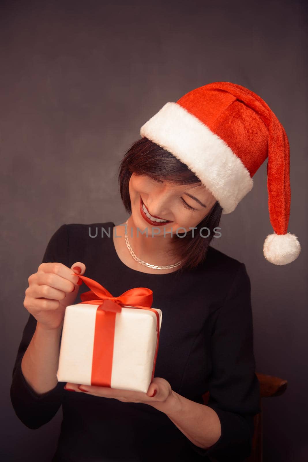Happy woman in santa hat is opening a gift box with red bow