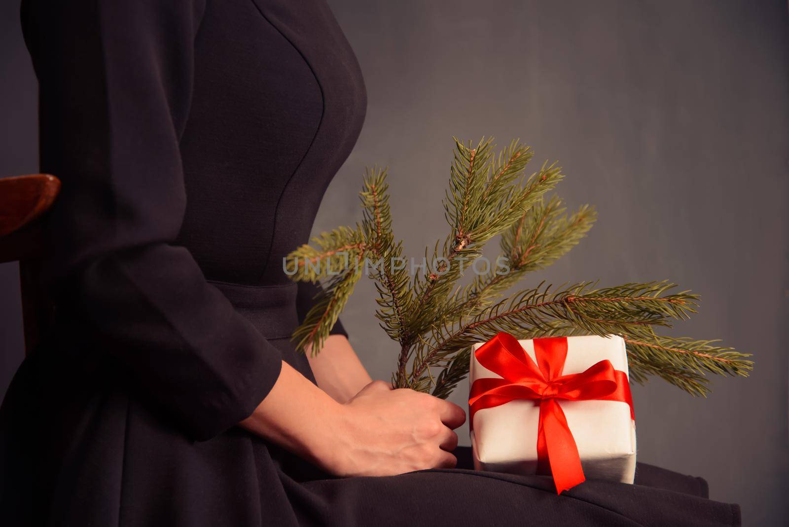 Unrecognizable woman is holding branch of Christmas tree and present, side view