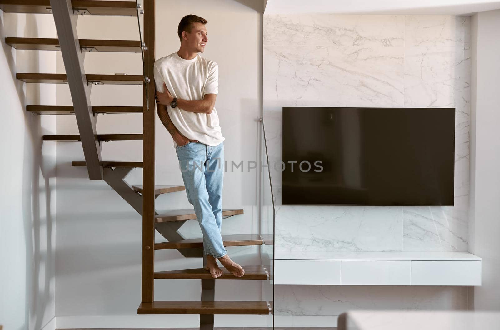 Relaxing happy caucasian man on the minimalistic stairs in modern light apartment by Yaroslav_astakhov