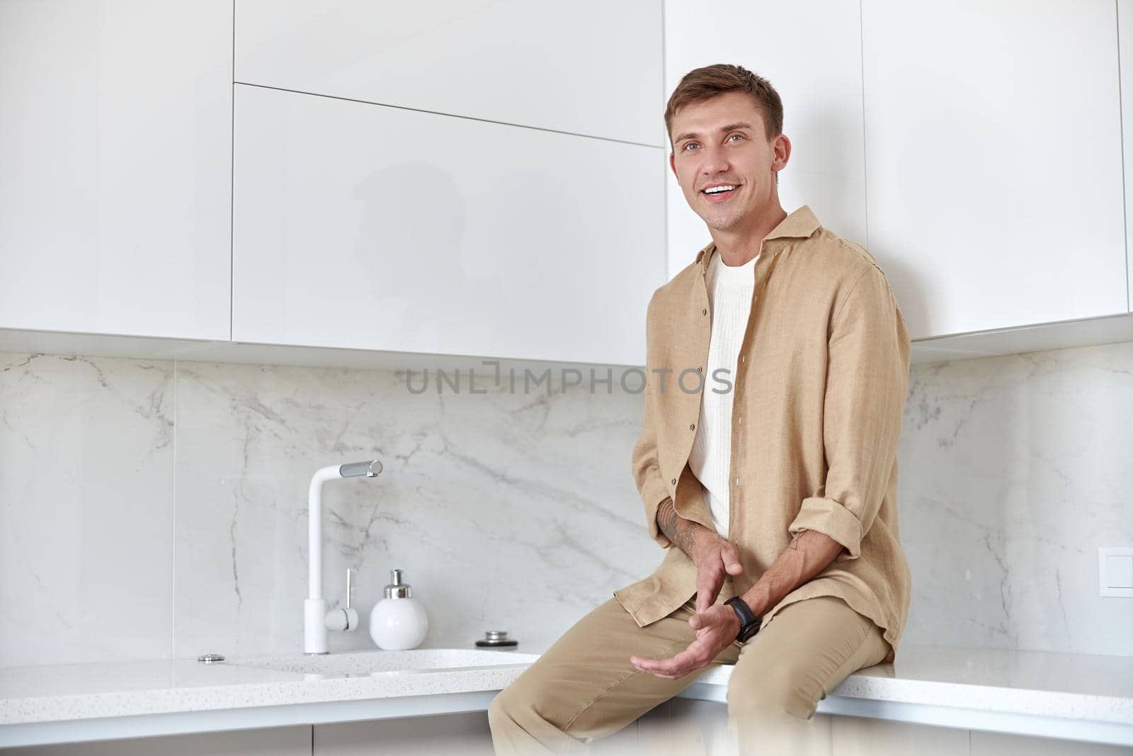 Happy handsome man is standing on minimalistic kitchen and smiling