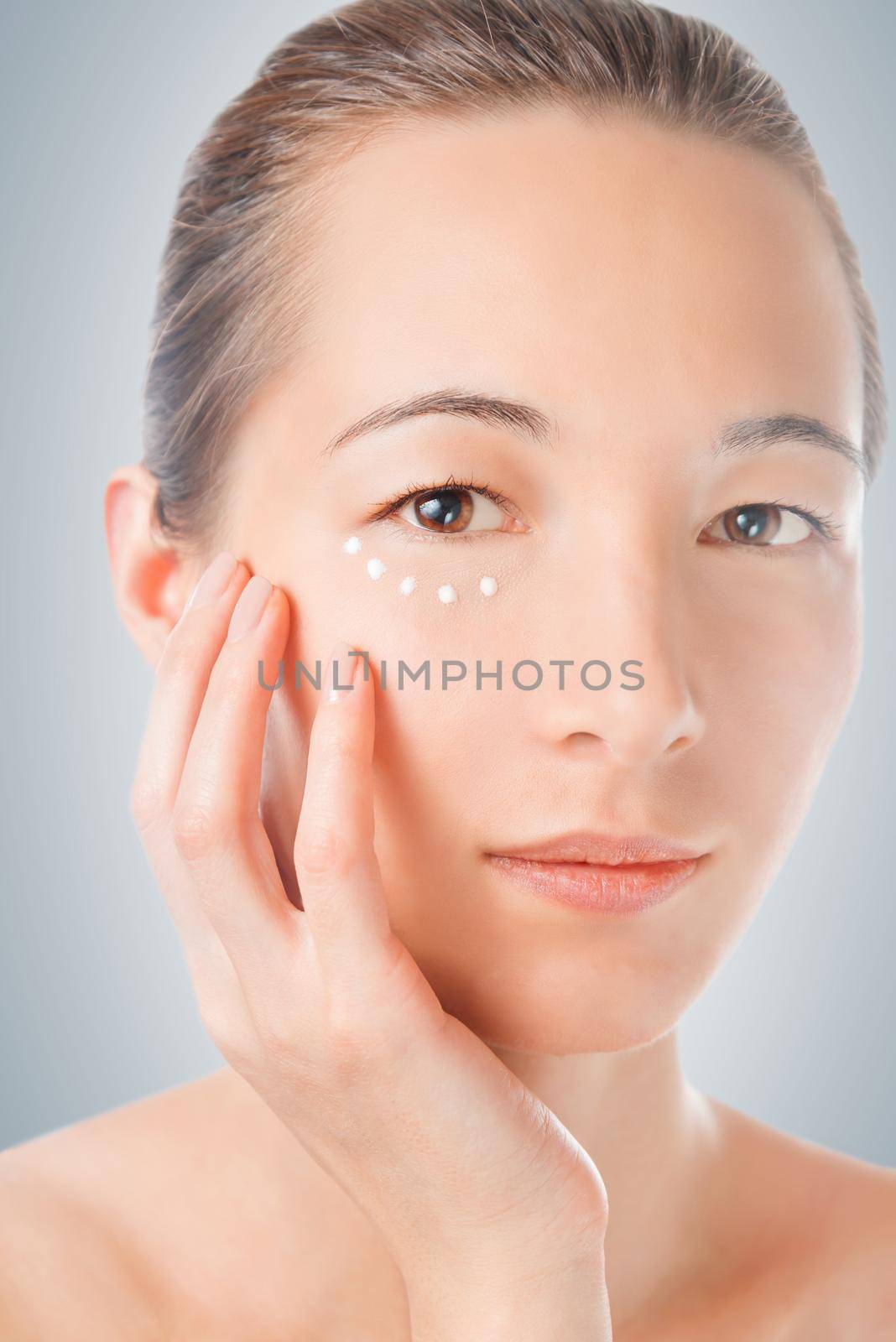 Beautiful woman touches face, applying cream on her skin around eye