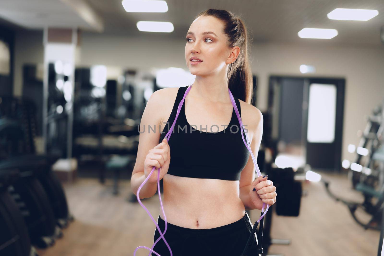 Portrait of a pretty fit girl with jumping rope standing in a gym