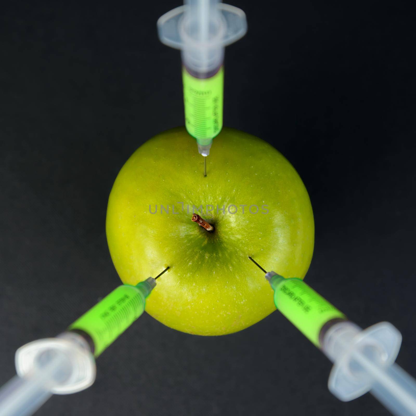 Red modification liquid in the syringe injected into green apple, top view