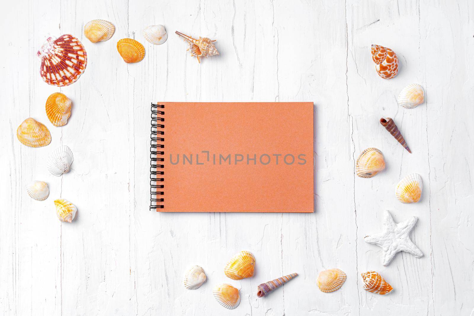 Open notepad with sea shells on white wooden background, top view