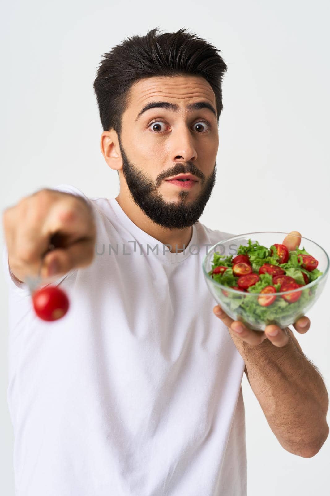 Cheerful man in a white T-shirt with a plate of light green and a healthy meal. High quality photo