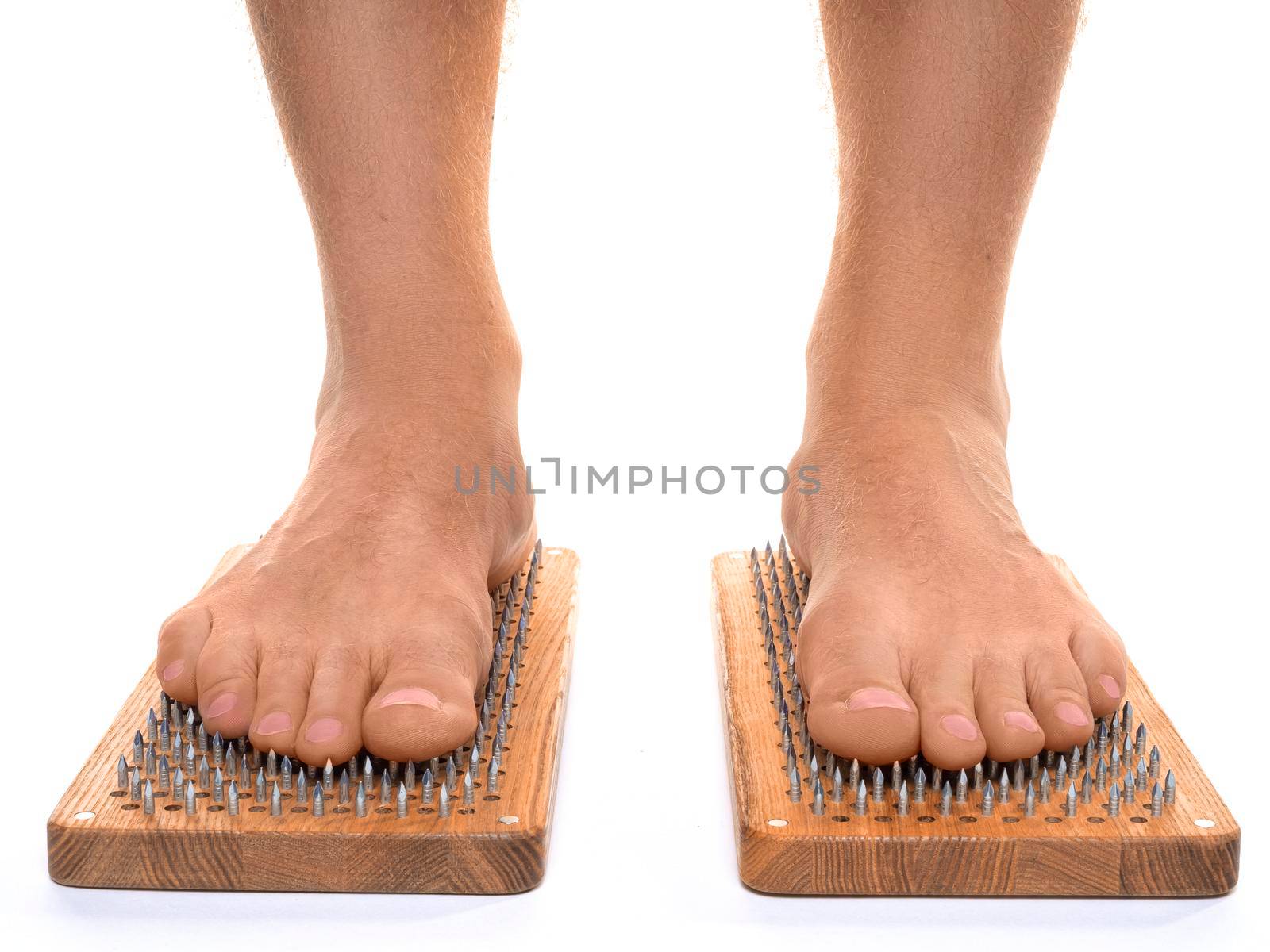 Front view of a male feet stand on a board with sharp nails over white background. Sadhu's board - practice yoga. Pain, trials, health, relaxation, cognition. Close-up.