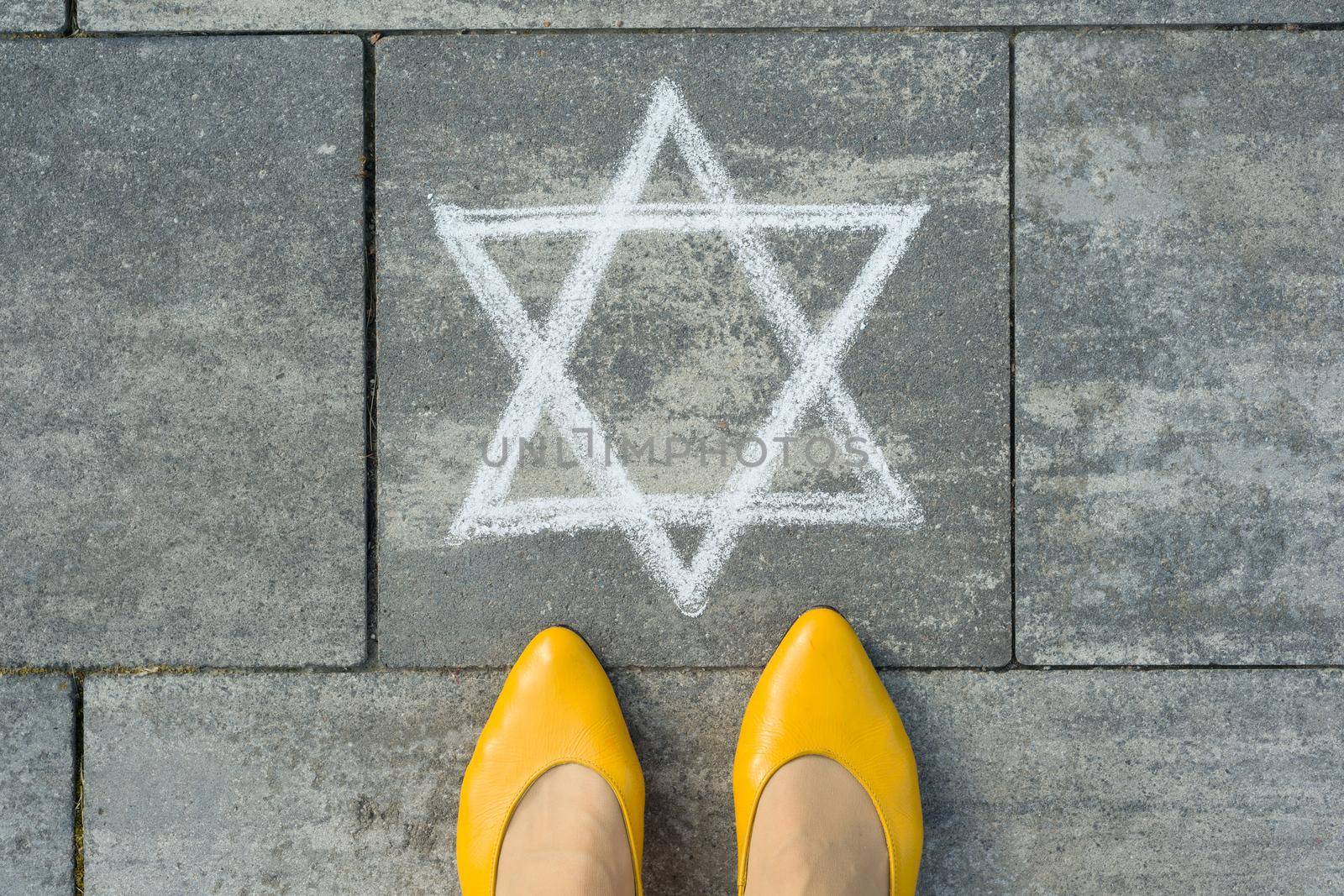 Female feet with abstract image of a six-pointed star, written on grey sidewalk