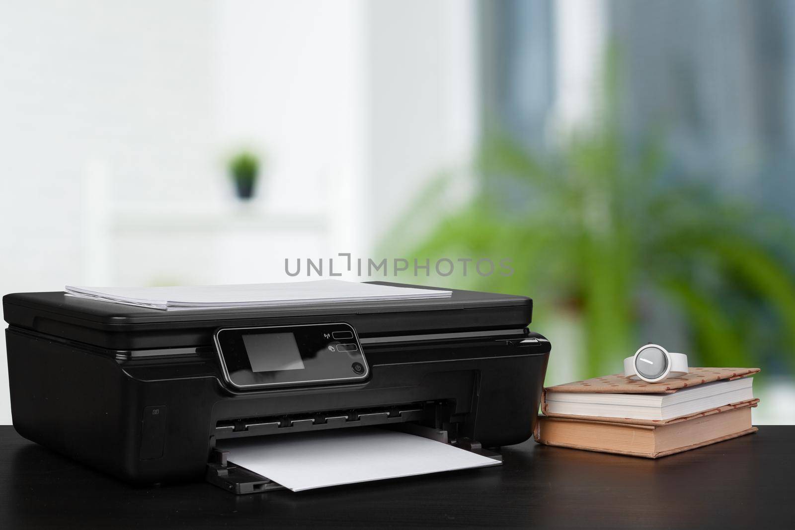 Stack of books and home printer against blurred background, close up