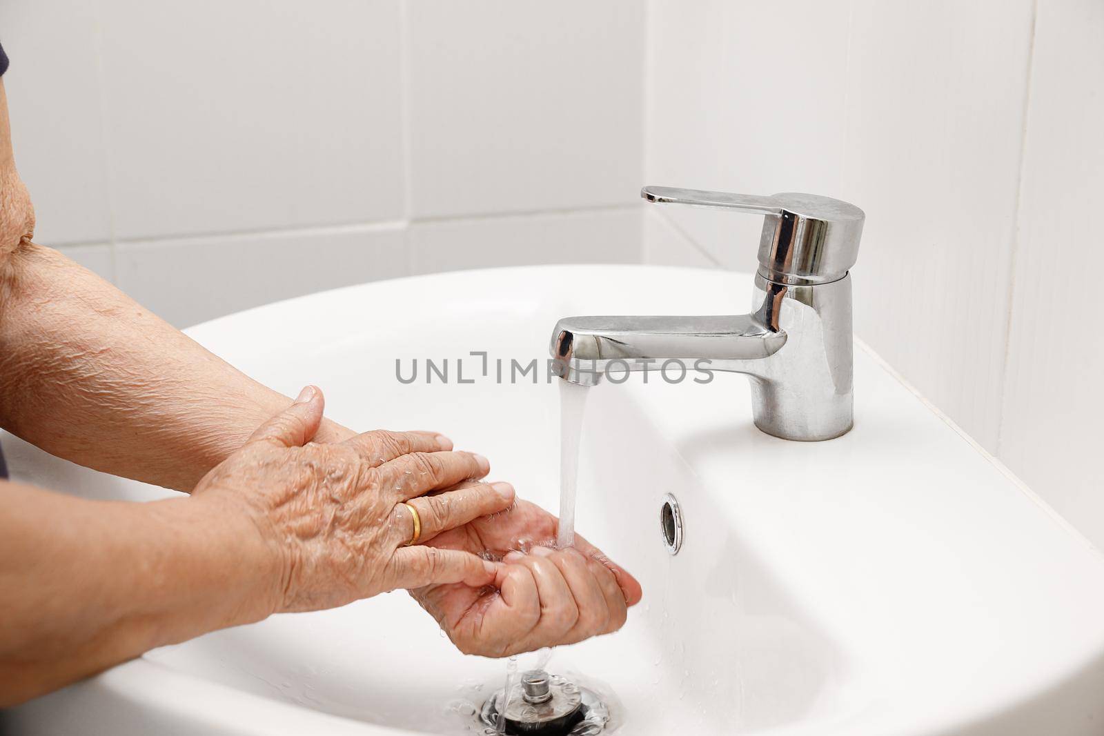 Elderly woman washes hand in bathroom