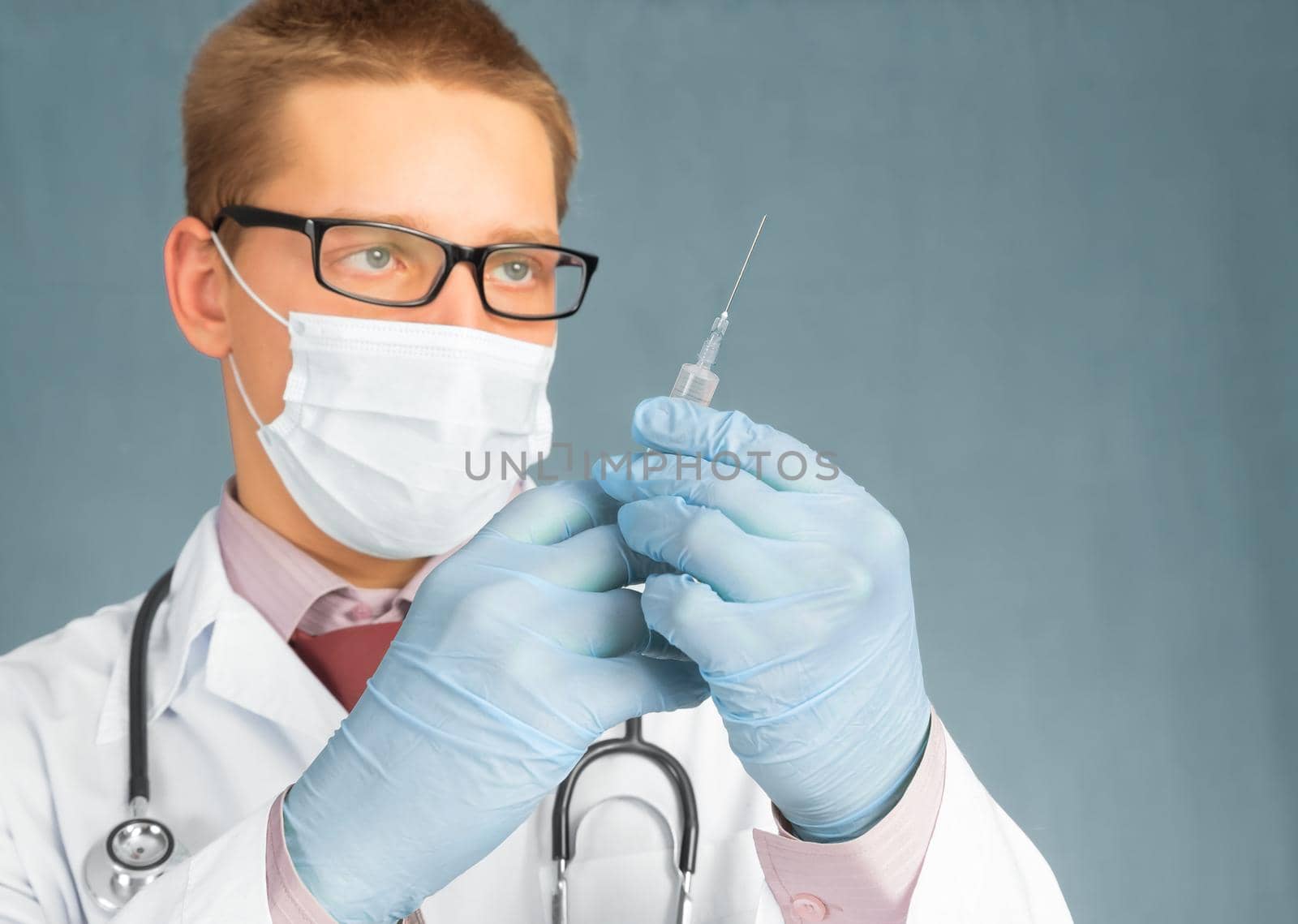 Man doctor in mask and gloves holds a syringe
