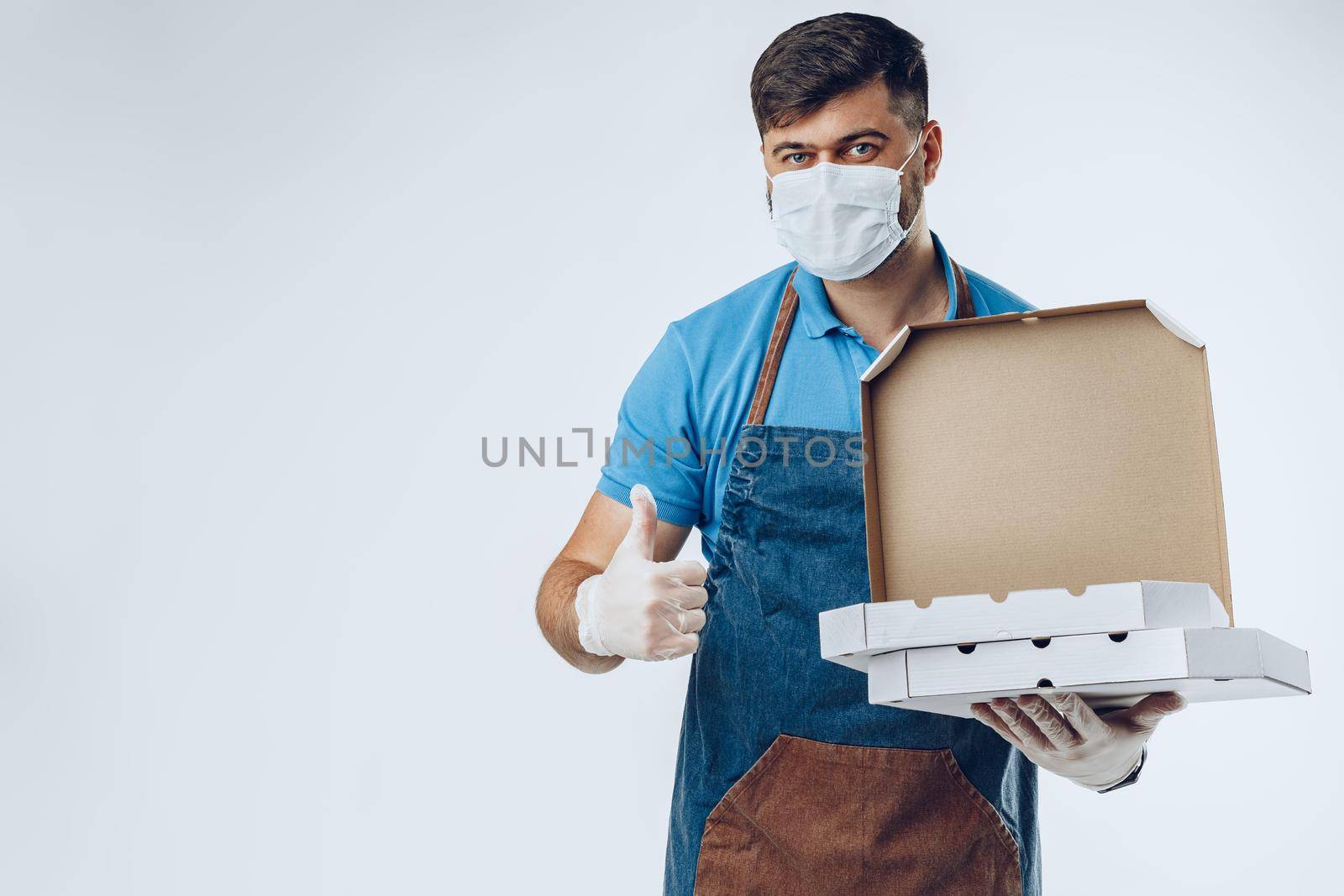 Pizza delivery man in medical gloves and mask against grey background. Safe service while coronavirus covid-19 outbreak