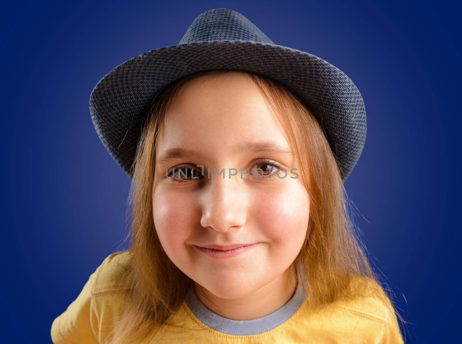Portrait of happy little girl in a hat on a blue background