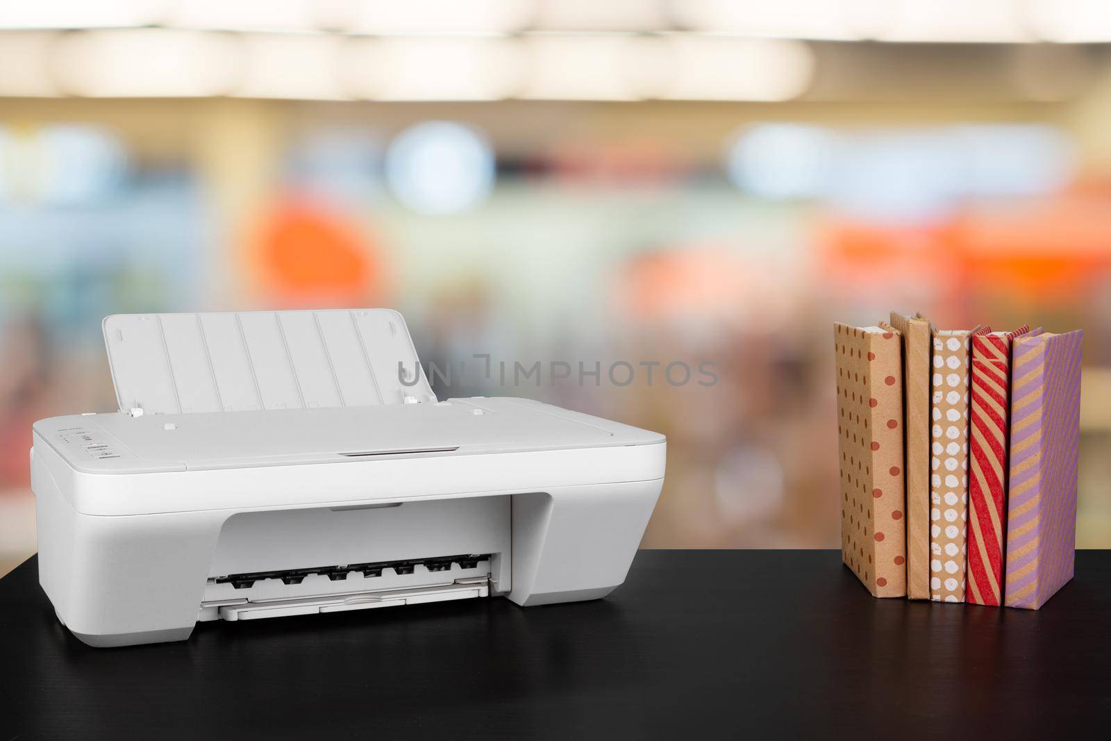 Compact home printer on desk with books against blurred background, close up