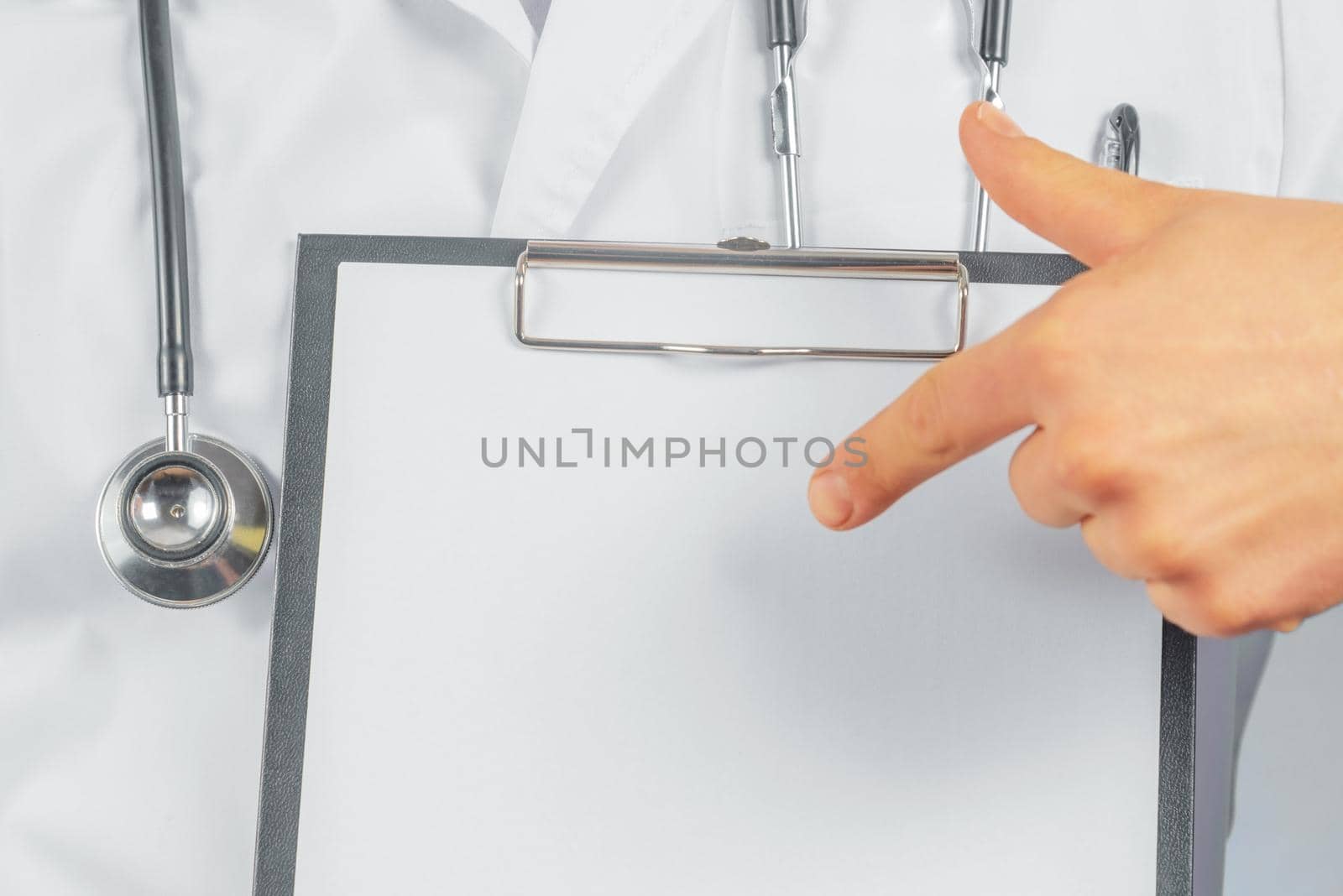 Unrecognizable man doctor is pointing on blank clipboard, space for text