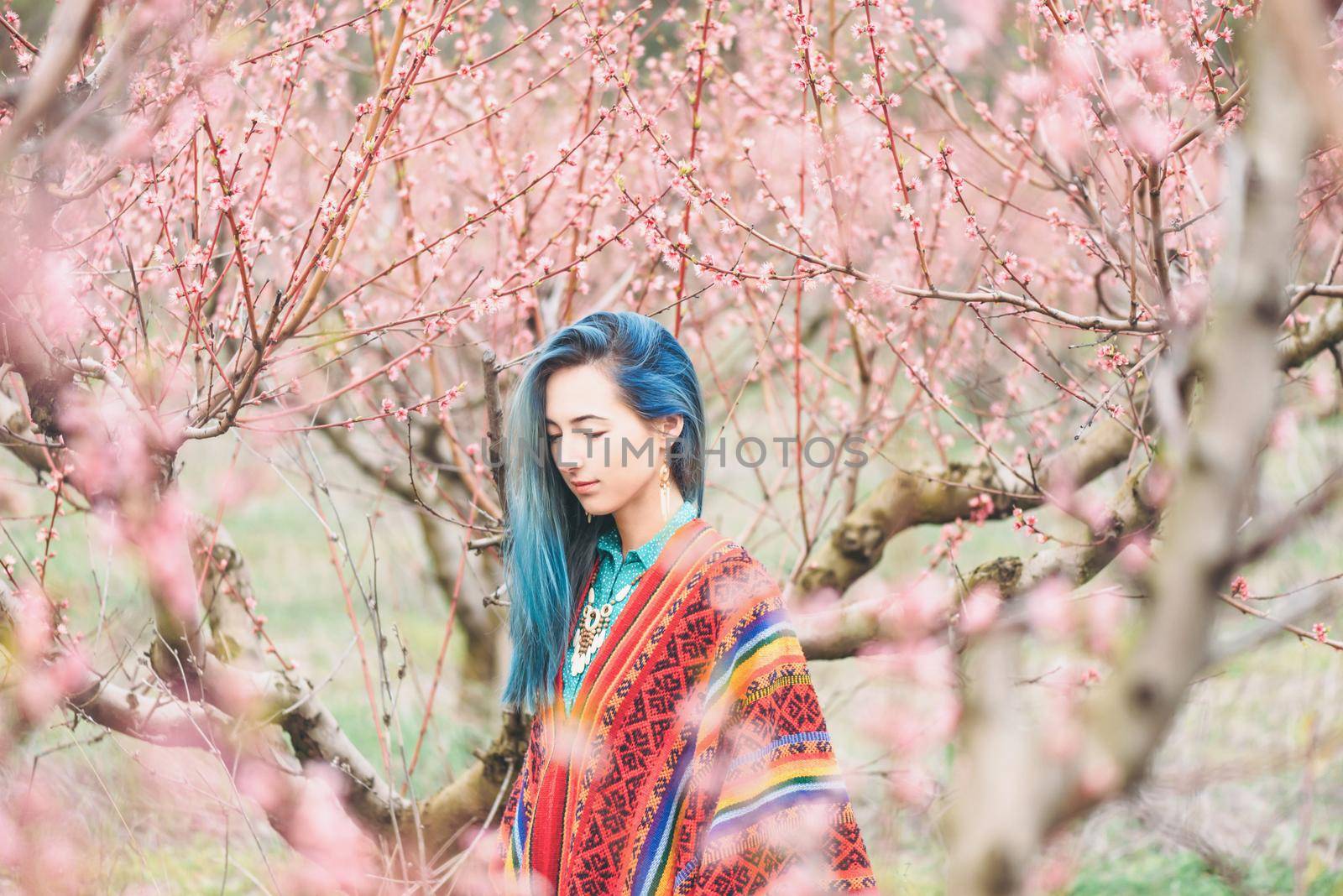 Boho style young woman walking in pink flowering peach tree garden