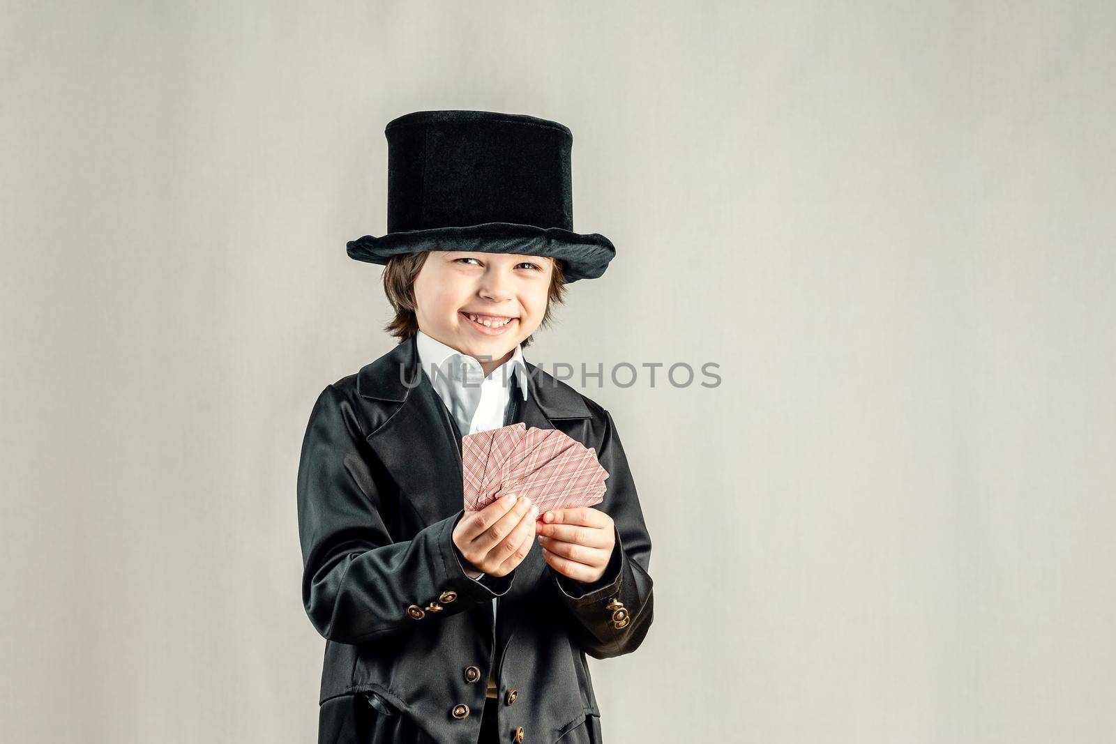 Young six year old boy wearing black suit and showing playing cards trick during illusionist performance. Cosplay, Retro party or Halloween costume concept.