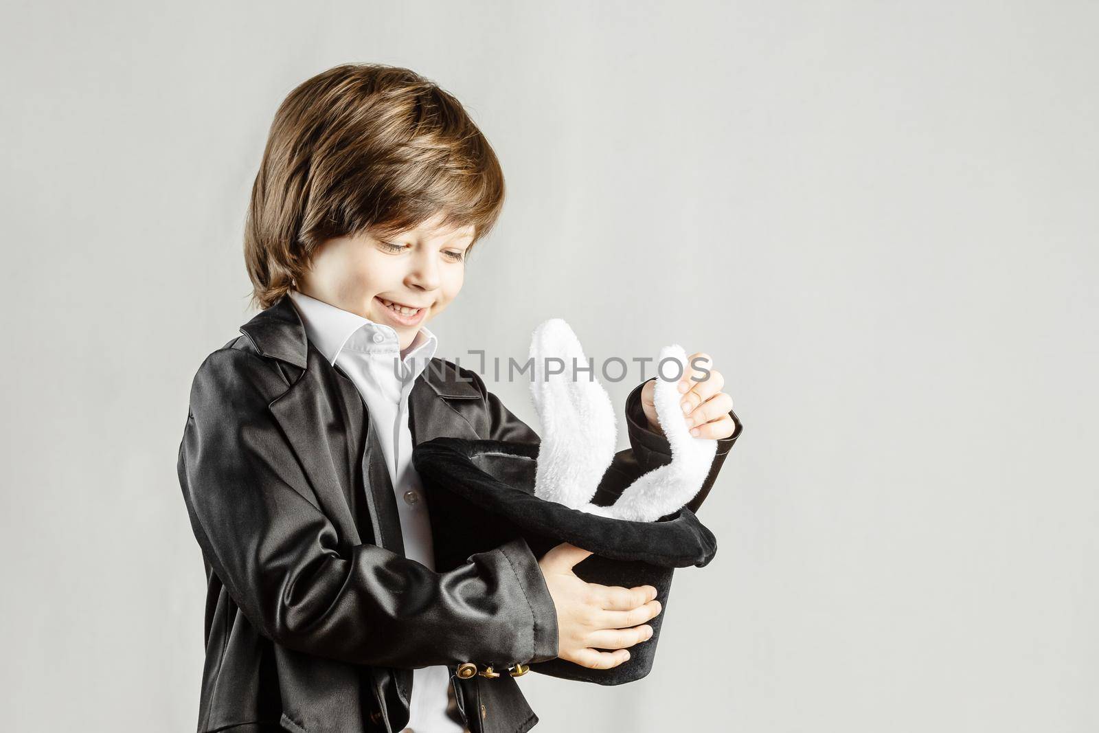 Adorable child dressed as an illusionist getting bunny from a hat over grey background