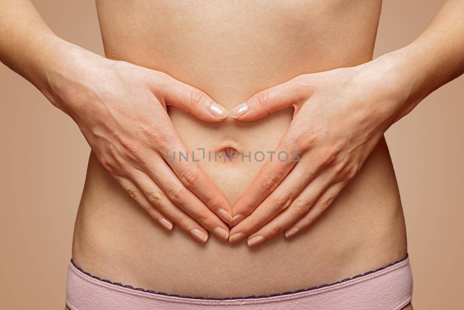 Unrecognizable woman holds her hands in heart shape in front of her abdomen