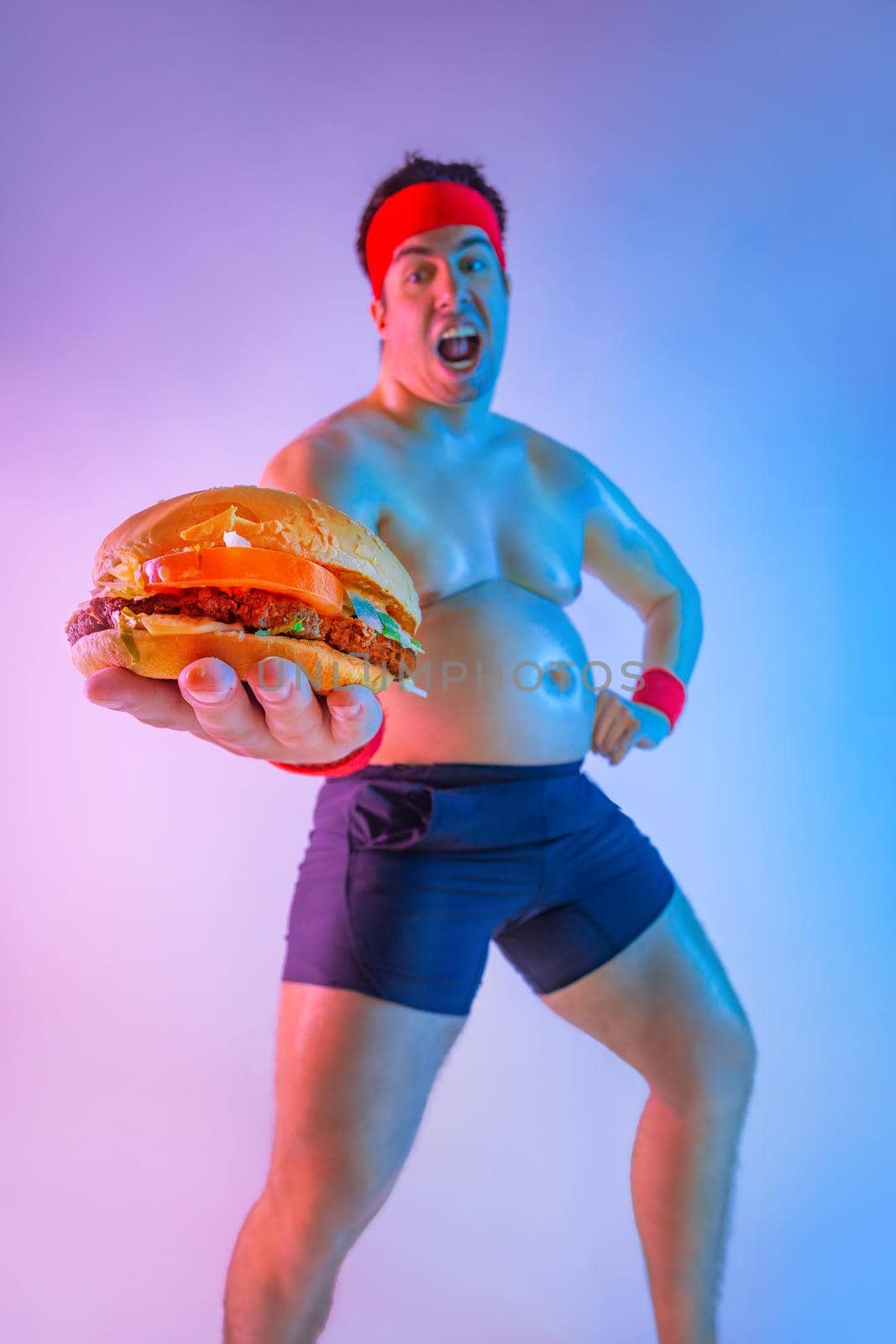 Fat man with gives away hamburger for lose weight and become a slim athlete. Not sporty male eating hamburger isolated on pink background