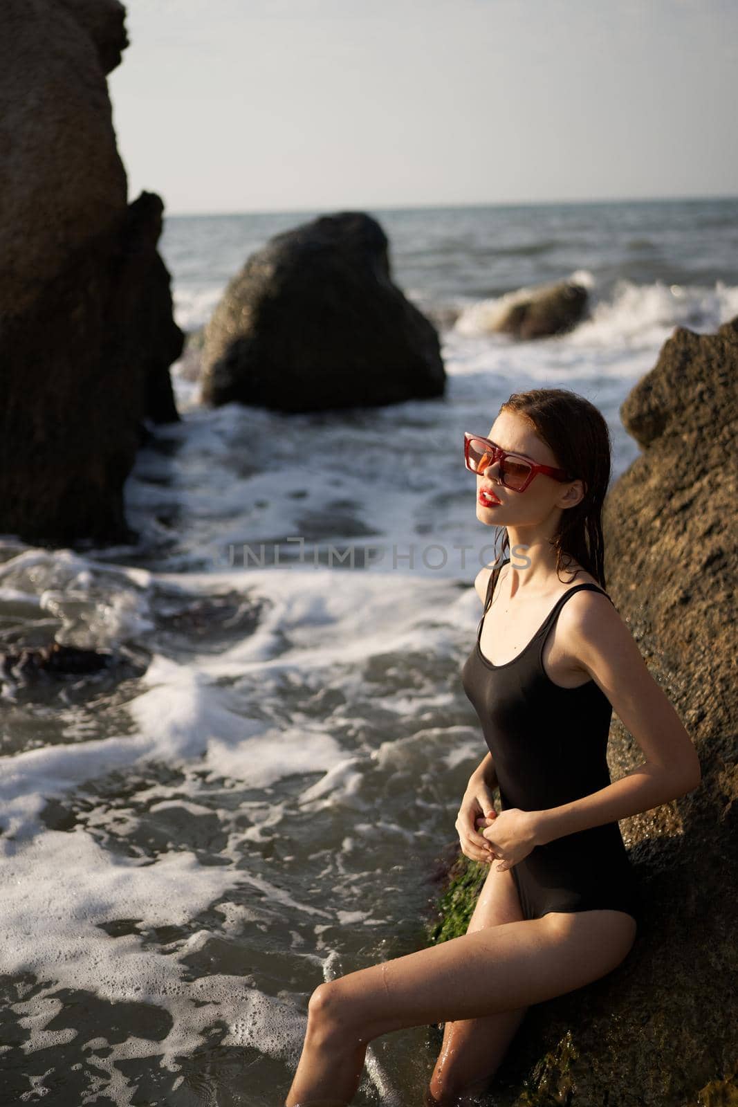 woman in swimsuit sunglasses ocean rocks posing. High quality photo