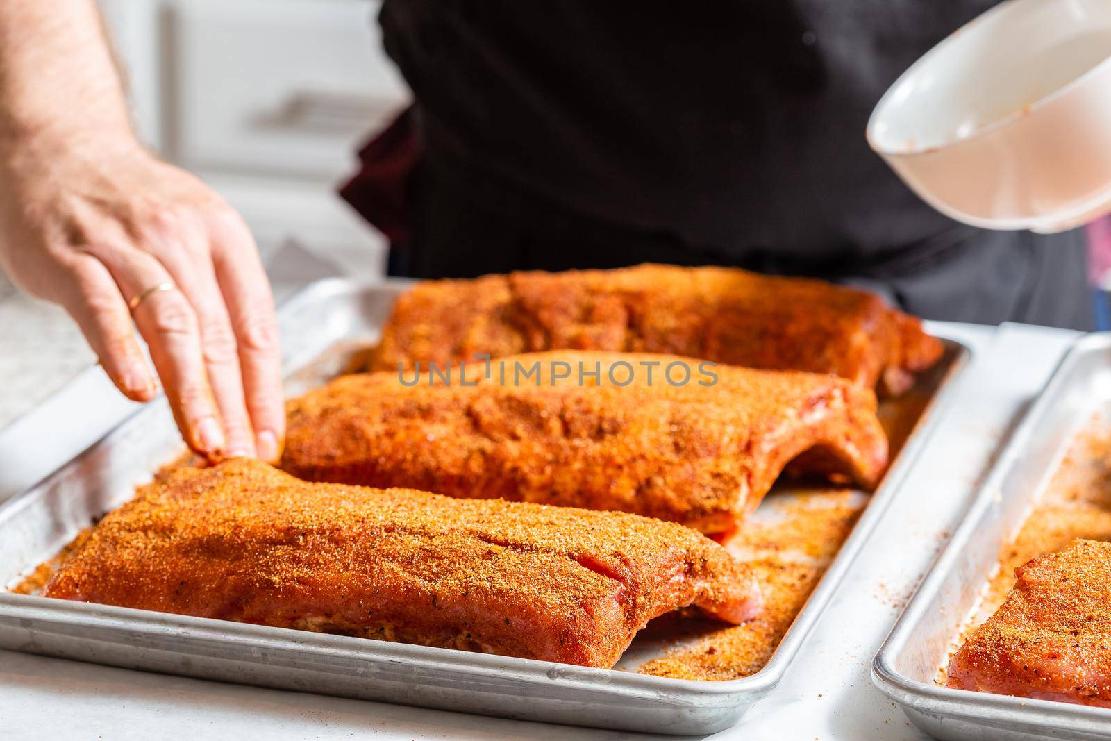 The hand of a male chef puts salt and spices on the raw piece of beef ribs meat. Raw St Louis Style BBQ Ribs with Rub Ready to Cook