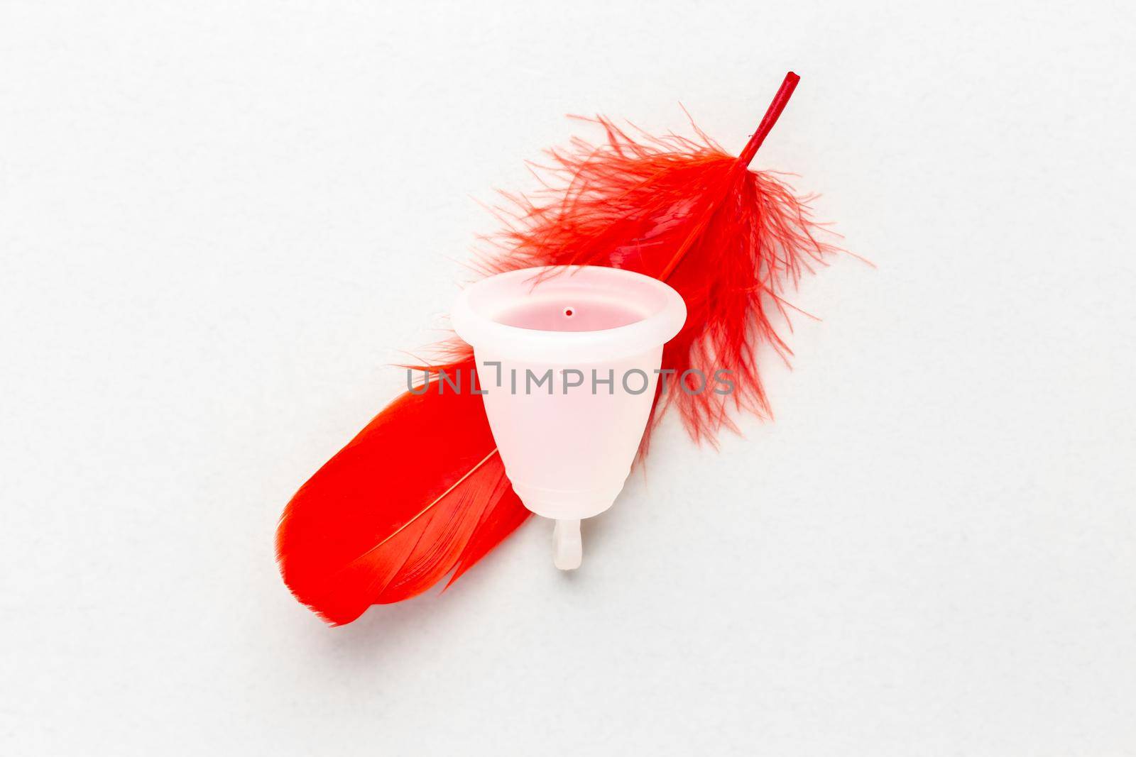 Menstrual cup with red feather over grey background. Periods hygiene product, zero waste alternatives