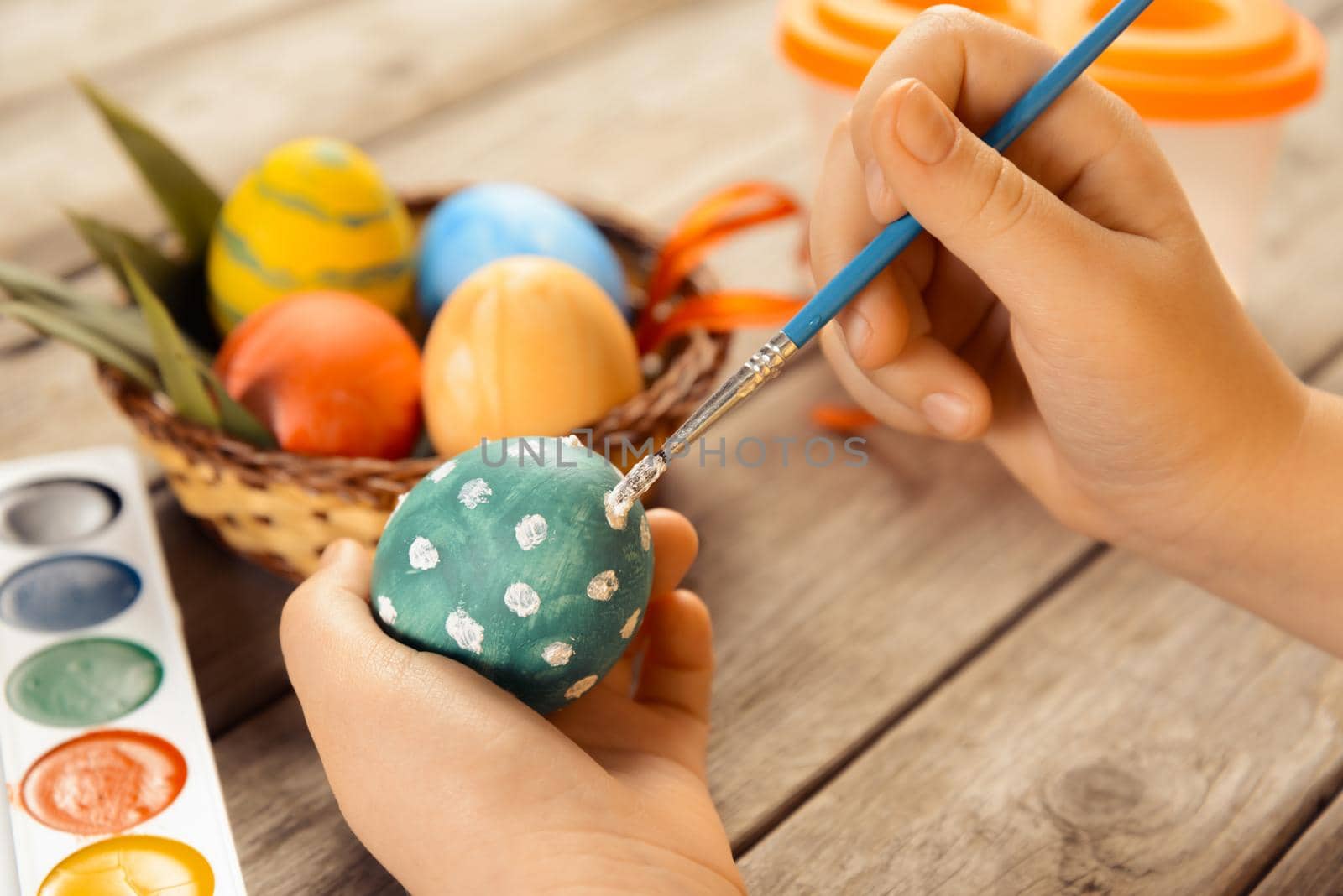 Female child paints egg for Easter on a wooden background, side view