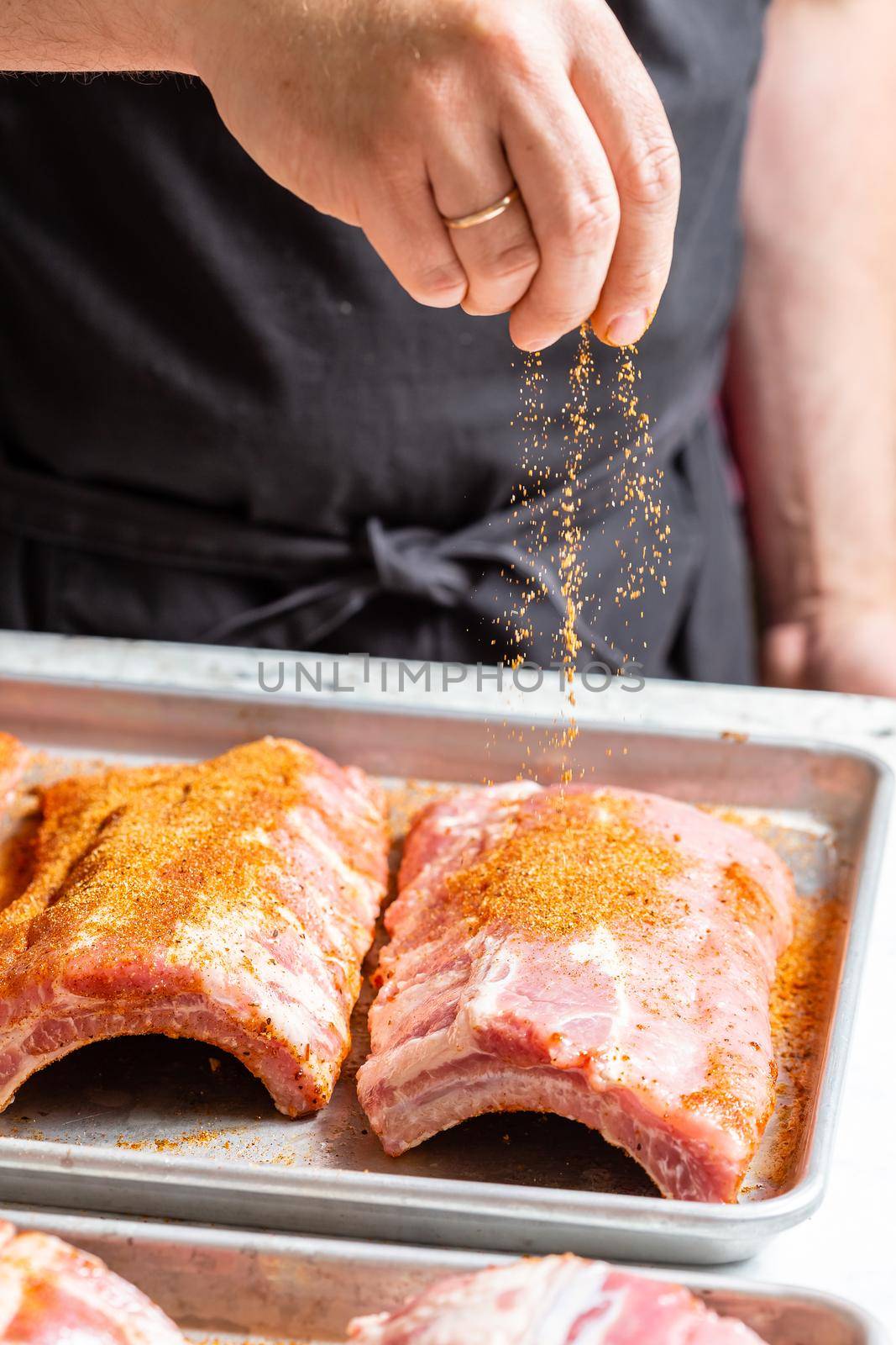 The hand of a male chef puts salt and spices on the raw piece of beef ribs meat. Raw St Louis Style BBQ Ribs preparation process