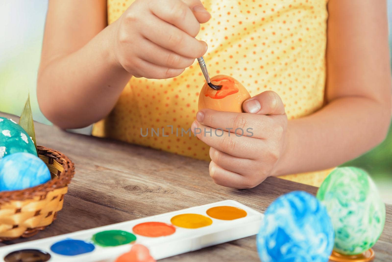 Little girl paints egg in orange color for Easter day, face is not visible