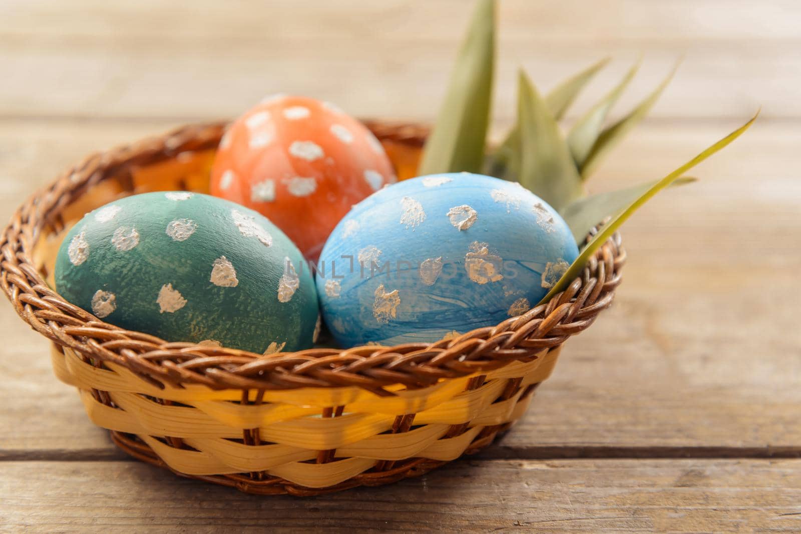 Three Easter colored eggs in a small basket on a wooden table