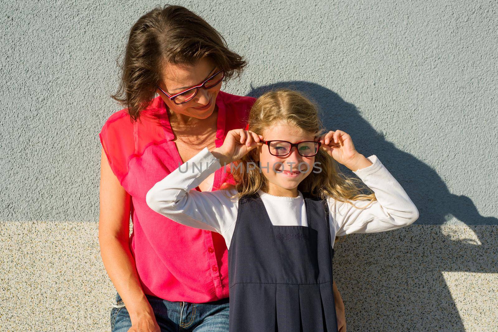 Mom and her little daughter, a student, enjoy socializing. The girl smiles and adjusts her glasses. Back to school!