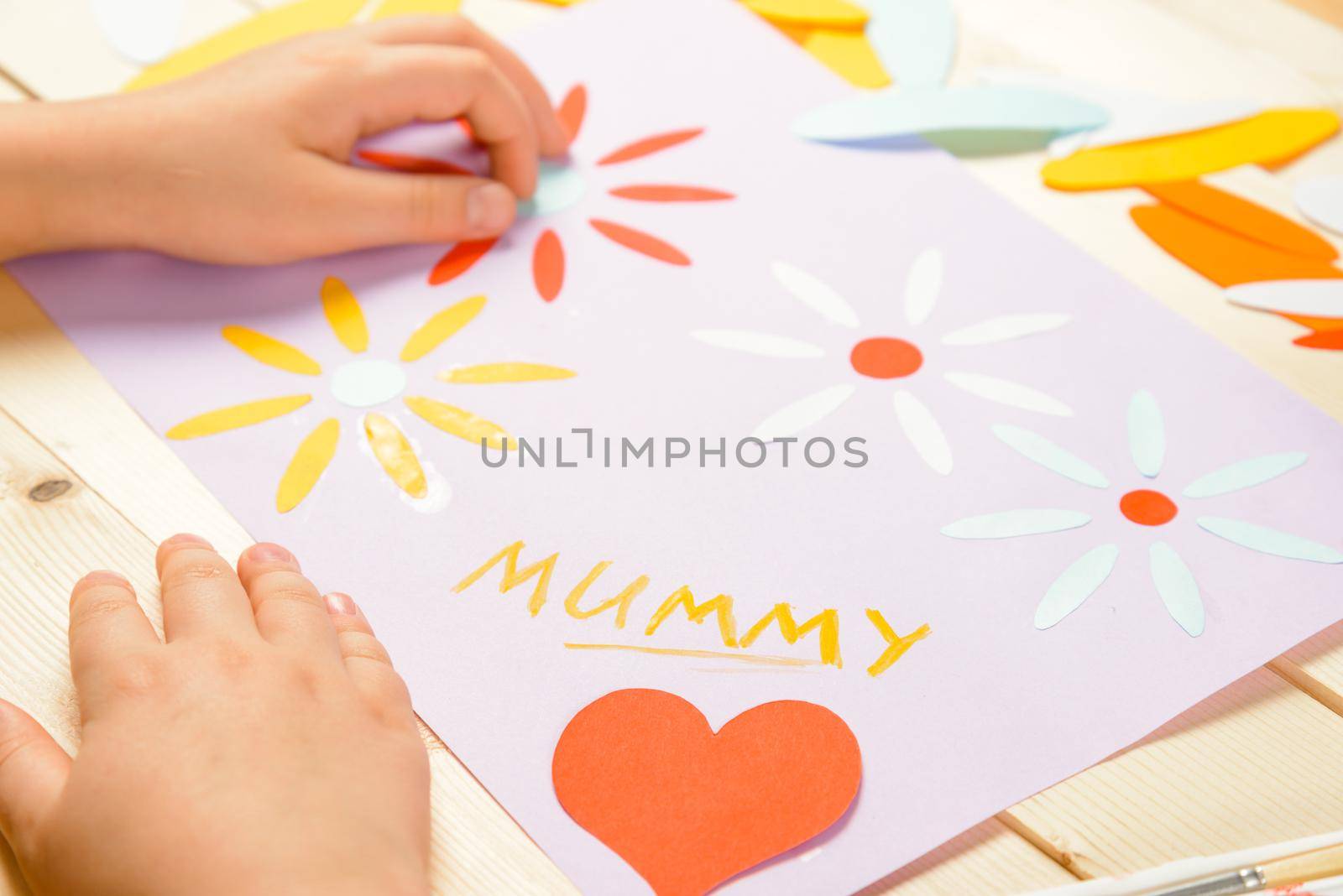 Unrecognizable little girl makes a greeting card for mother on holiday