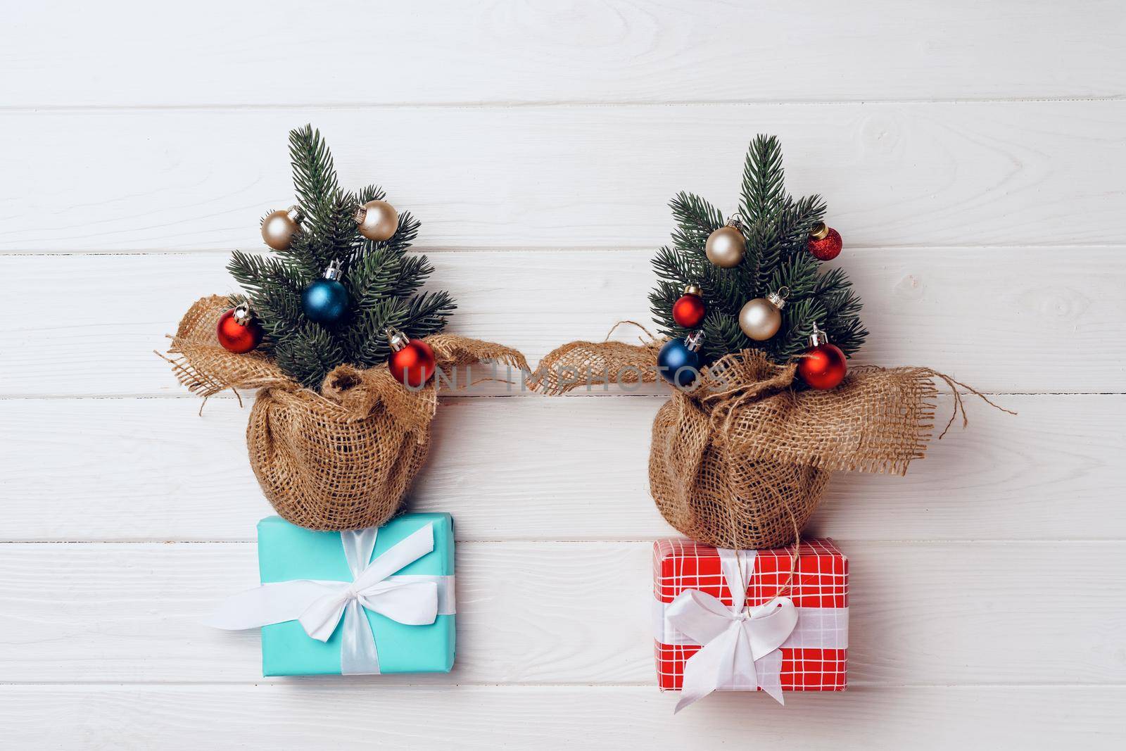 Pine tree decorated with baubles and wrapped Christmas gifts on white wooden background top view