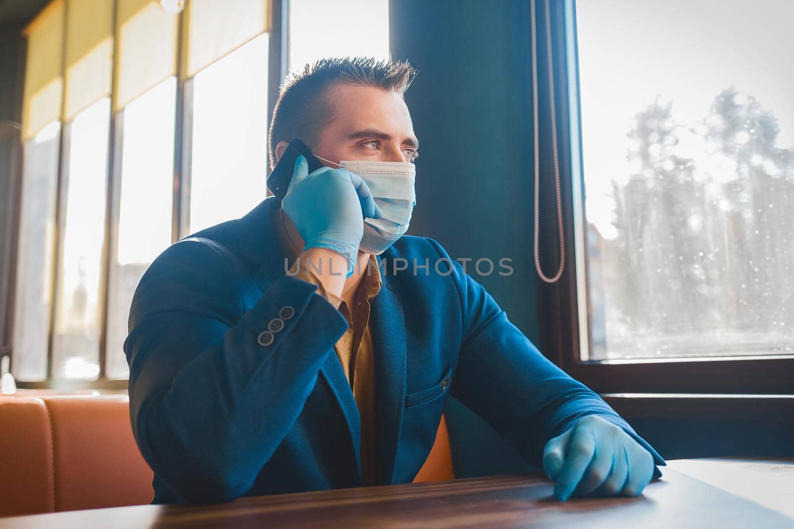 Young caucasian guy businessman in protective gloves and a medical mask talking on the phone and looking out the window.
