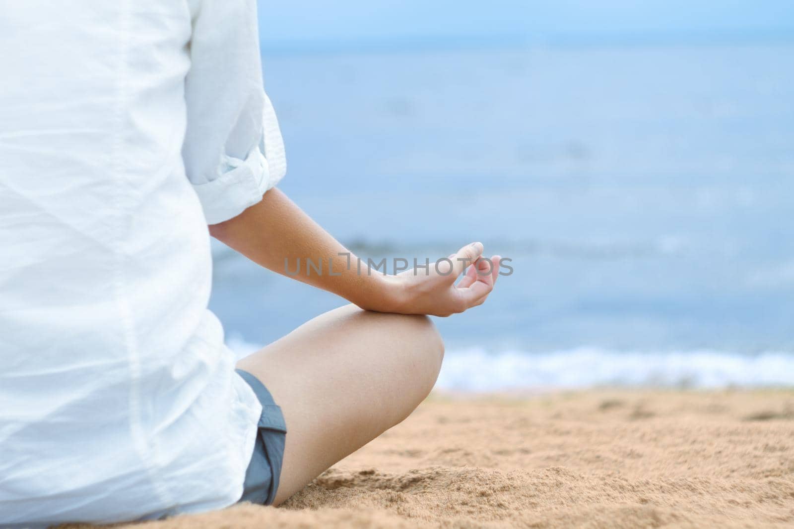 Young woman meditating in lotus position while sitting on beach