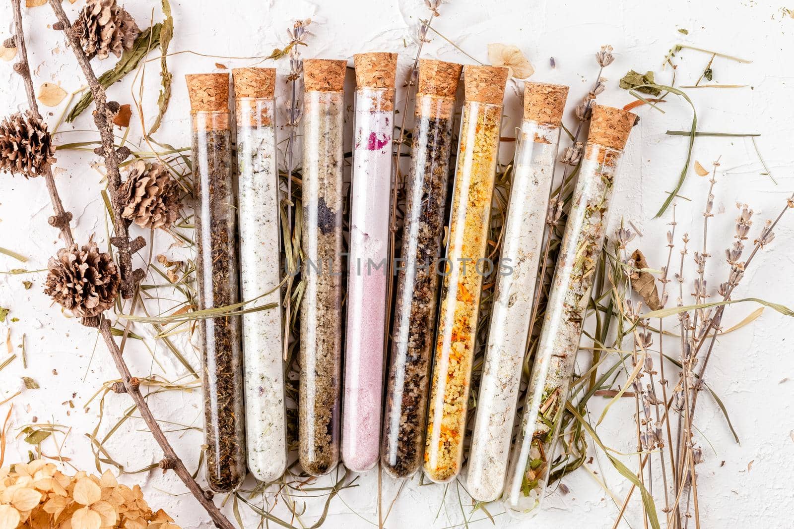 Variety of bath salts in glass tubes with dry herbs around. Natural organic SPA cosmetic product. Skin care, beauty treatment concept