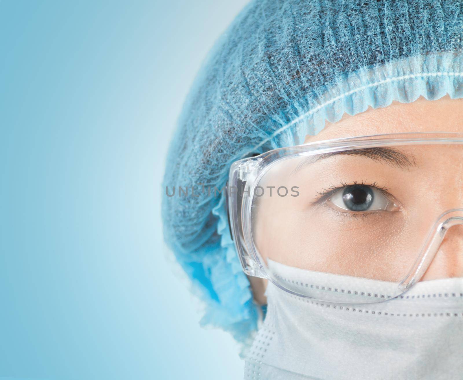 Young woman surgeon in cap, glasses and mask looks at camera, close-up